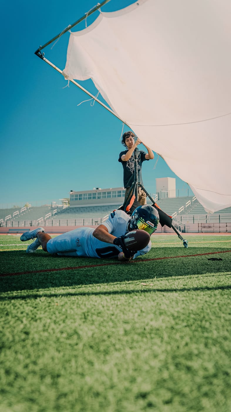 Football player diving with the ball while a crew member holds a large diffusion frame